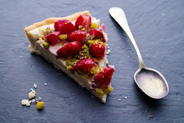 Strawberry tart slice with pistachios, rustic silver spoon and c