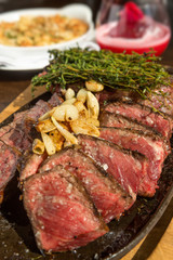 A selection of grilledT Bone steak pieces and roasted garlic, off the bone on a metal plate