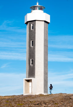Grey lighthouse made of concrete with person walking next to it