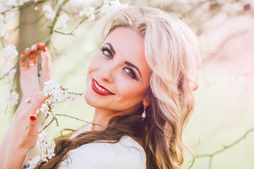 Obraz na płótnie Canvas Close Up of Beautiful Blond Woman Looking Up and Smiling Underneath Tree Branches Filled with White Blossoms Outdoors in Spring Time