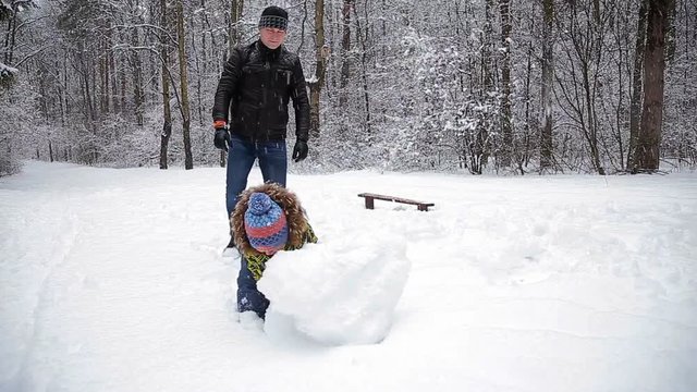 Father and young son make a snowman in winter park