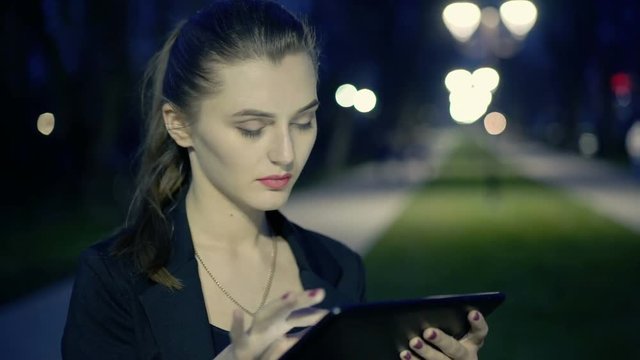 Beautiful girl enjoys the tablet at night