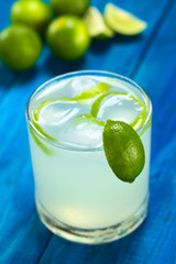 Freshly prepared refreshing lemonade out of limes with ice cubes and lime zest (Selective Focus, Focus on the lime wedge on the rim)