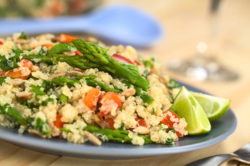 Vegetarian quinoa dish with green asparagus and red bell pepper, sprinkled with parsley and roasted sunflower seeds, lime wedges on the side (Selective Focus, Focus on the asparagus heads on the dish)