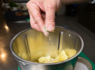 Close up shot of a hand dropping black pepper onto fluffy peeled potatoes into a blender.