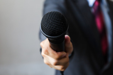Man in business suit holding a microphone conducting a business interview, journalist reporting,...