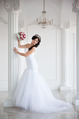 Beautiful brunette bride in a wedding dress and a crown on her head, full-length portrait. Interior with columns.