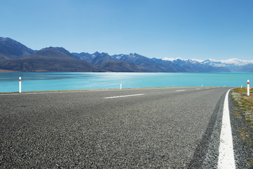 empty asphalt road near water and snow mountains