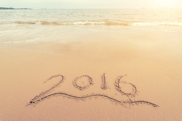 Year 2016 hand written on the white sand in front of the sea