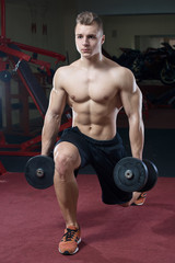 Fototapeta na wymiar Muscular man topless doing lunges with dumbbells in a black shorts in the gym