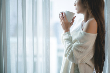 Fototapeta premium Cropped image of woman wit a big cup of coffee standing at window