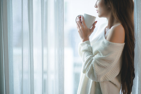 Cropped image of woman wit a big cup of coffee standing at window