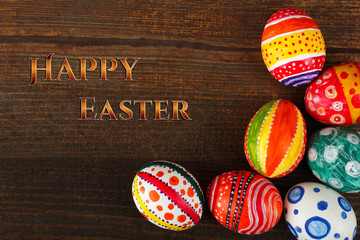 Easter eggs in beautiful and different colors lie on a wooden background with the words 