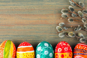 Easter eggs painted in different colors near willow twigs on wooden background