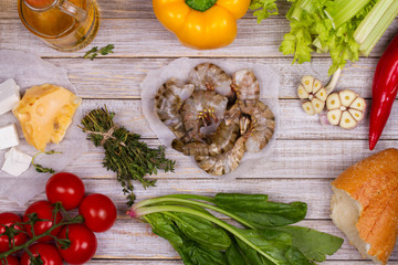 Overhead View of Shrimps, Spinach, Bell Pepper, Tomato Cherry, Bread, Garlic, Thyme, Olive Oil, Glass of White Wine, Celery and Feta Cheese on Rustic Wooden Background