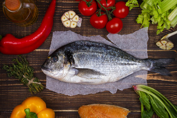 Overhead View of Dorado Fish, Spinach, Bell Pepper, Tomato Cherry, Bread, Garlic, Thyme, Olive Oil, Glass of White Wine and Celery on Dark Rustic Wooden Background