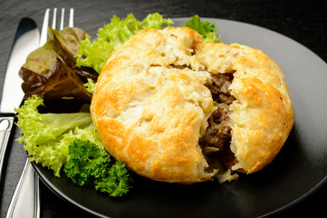 Pie with minced meat on black plate.