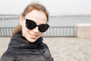 Happy smiling girl in sunglasses. Woman walking at city waterfront.