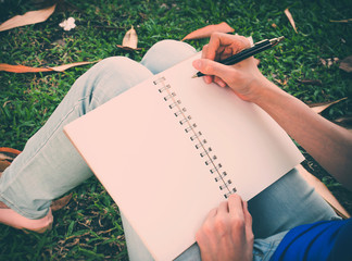 Young woman sitting in the park writing something in the book