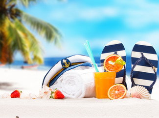 Orange juice and summer accessories on sand with tropical beach background