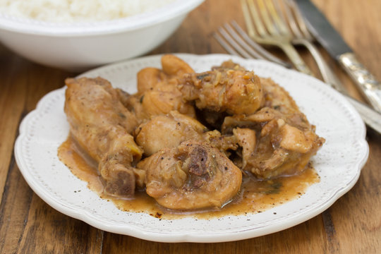 boiled chicken with beer sauce in white plate and rice in bowl on brown wooden background