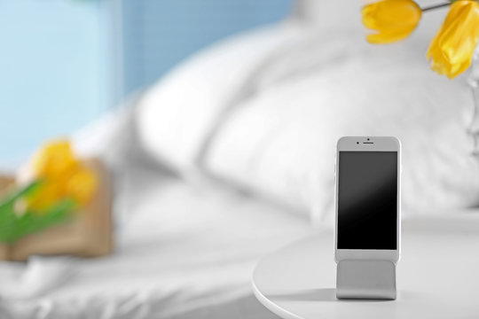Smart Phone With Stand On A Bedside Table In A Room