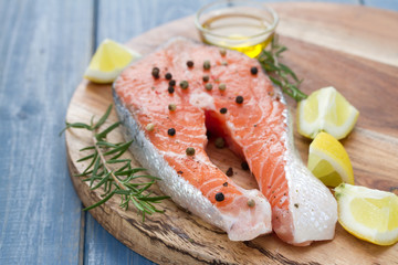 fresh salmon with lemon, oil and rosemary on wooden board on white background
