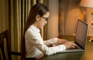 Girl in school uniform sitting behind table and using laptop at