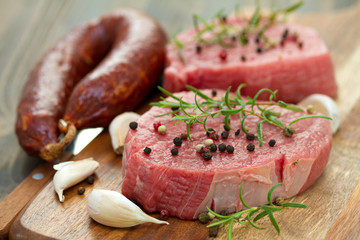 raw meat with smoked sausage, pepper and garlic on wooden board on brown background