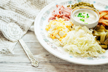 
salad with lots of ingredients - roasted potatoes, green peas , boiled eggs , ham , cabbage , pickled cucumbers , green onions , and mayonnaise on a wooden background 