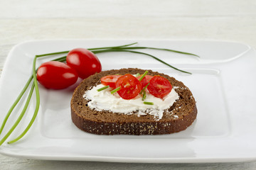 slice of pumpernickel bread with cream cheese amd tomato slices