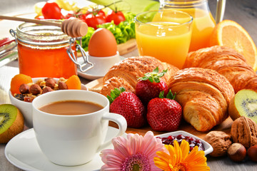 Breakfast consisting of croissants, coffee, fruits, orange juice