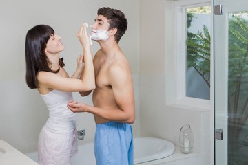 Young woman applying shaving cream on young mans face
