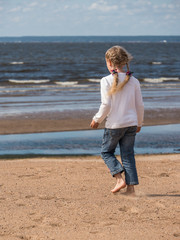 a little blonde girl walking along baltic seashore