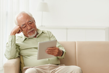 Old man reading book on tablet computer at home