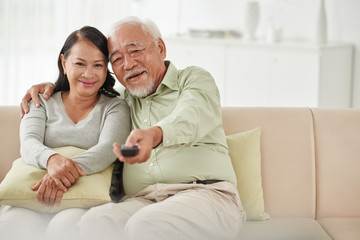 Smiling senior couple watching tv at home