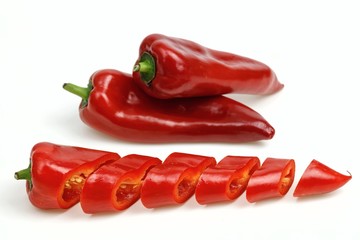 Pointy red peppers and one cut into pieces, on white background.