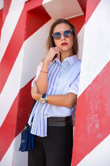 Fashion  girl posing over Red white striped wall background. Beauty woman with pink lips make-up posing on the street. 