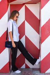 Fashion  girl posing over Red white striped wall background. Beauty woman with pink lips make-up posing on the street. 
