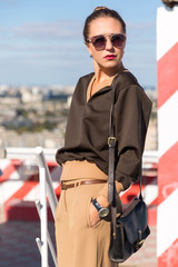 Street fashion portrait stylish pretty woman with sunglasses and bag posing in city on evening sunny sunset 