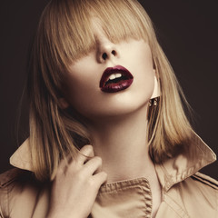 Fototapeta premium Beautiful blonde woman in a bright coat and dark lips, showing d