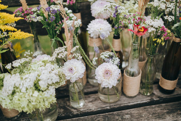 flowers and herbs in glass bottles standing on an old wooden bench in the garden