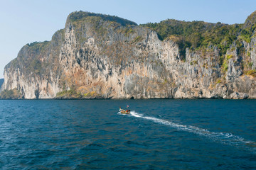 Fototapeta na wymiar Speed boat driving on blue water past rocky hills of Thailand