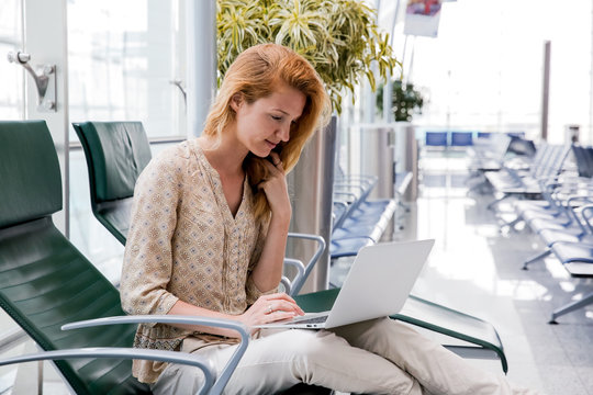 Casual business woman working on laptop in airport hall. Woman waiting his flight at airport terminal, sitting on chair and typing on the laptop.