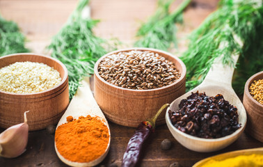 Beautiful colorful spices in wooden spoons and bowls on an old wooden brown table with green dill