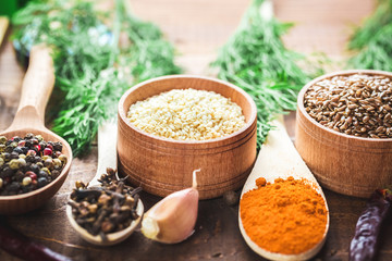 Beautiful colorful spices in wooden spoons and bowls on an old wooden brown table with green dill