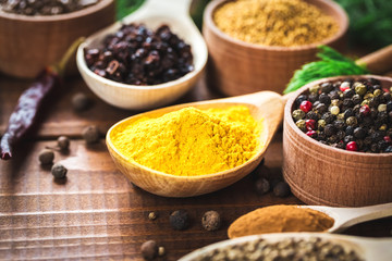 Beautiful colorful spices in wooden spoons and bowls on an old wooden brown table with green dill