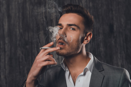 Handsome brutal man in gray suit smoking a cigarette
