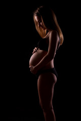 Obraz premium Young pregnant women in black underwear on black background is hugging her tummy
