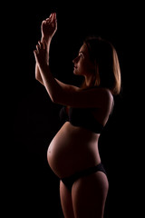 Young pregnant woman in black underwear is doing exercise on black background